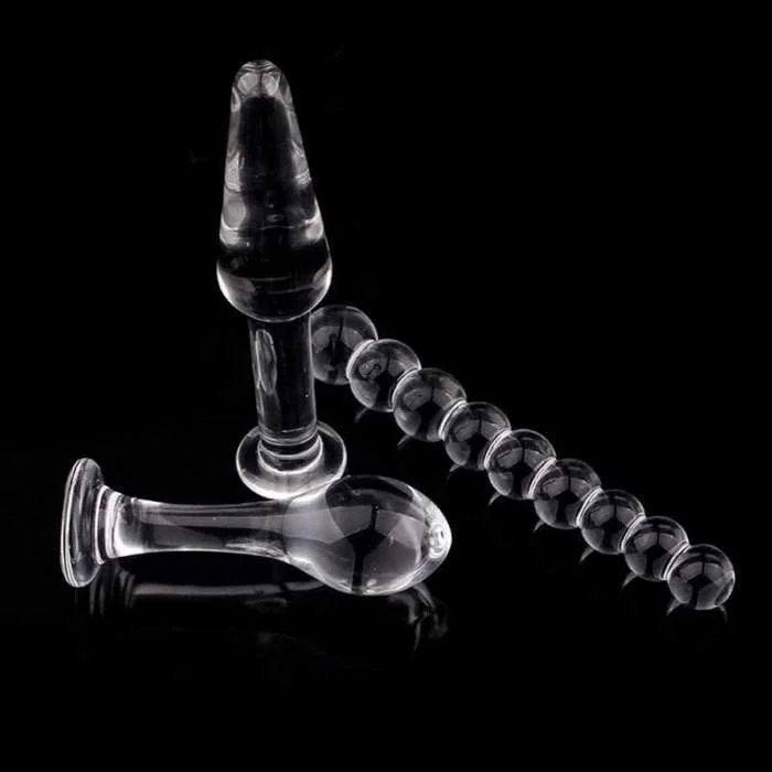 Τρία διαφανή γυάλινα sex toys διαφορετικού σχήματος πάνω σε μαύρη και ελαφρώς γυαλιστερή επιφάνεια.