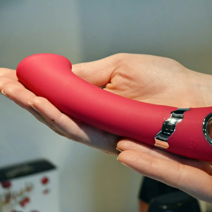 Χέρια κρατάνε κόκκινο G spot vibrator με κυρτή, διογκωμένη κεφαλή.