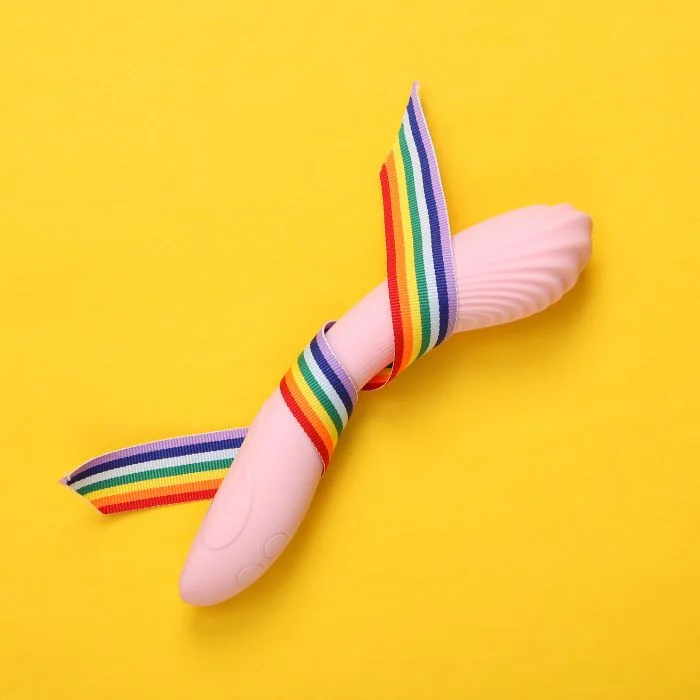Ροζ G spot vibrator με ανάγλυφη κεφαλή και rainbow κορδέλα, πάνω σε κίτρινο φόντο.