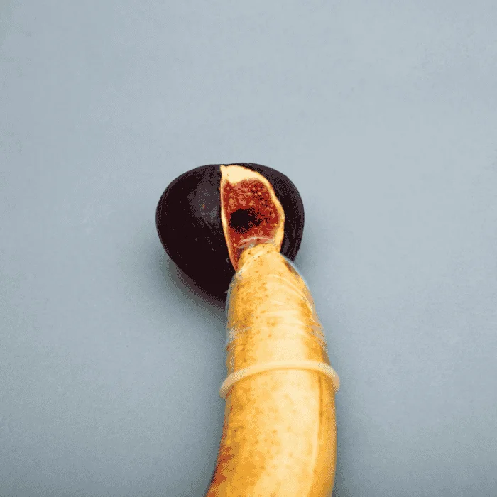 Μια κομμένη μπανάνα είναι συνδεδεμένη με ένα μισό σύκο, δεμένη με ένα λαστιχάκι, σε απλό γκρι φόντο.