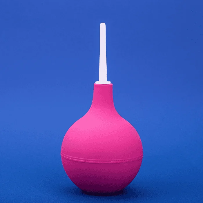 Φούξια πρωκτικό κλύσμα με λευκό ακροφύσιο τοποθετημένο κάθετα σε μονόχρωμο μπλε φόντο.