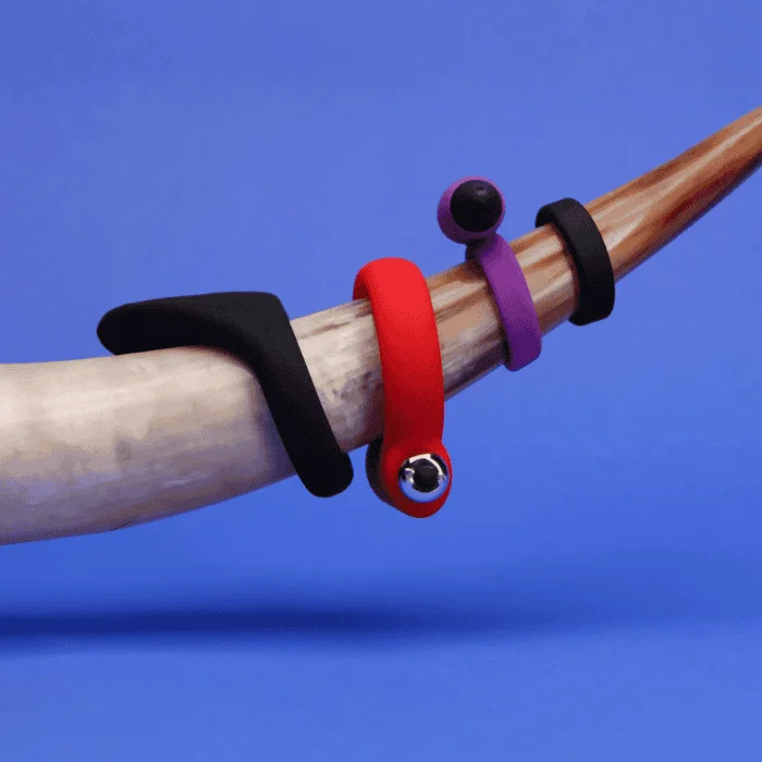 Τέσσερα δαχτυλίδια πέους με δόνηση σε μαύρο, κόκκινο και μωβ χρώμα, τοποθετημένα σε κέρατο με μπλε φόντο.