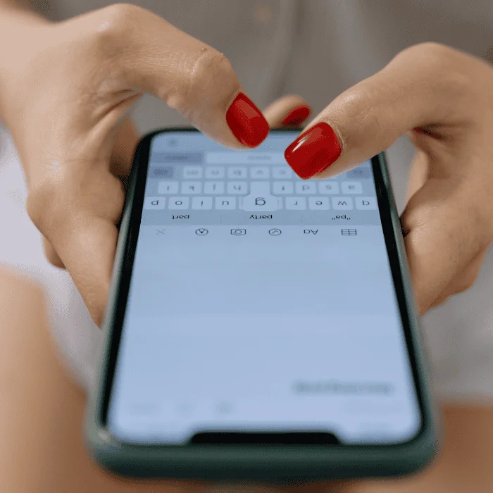 Χέρια με κόκκινα νύχια γράφουν σε κινητό με ανοιχτή εφαρμογή μηνυμάτων.