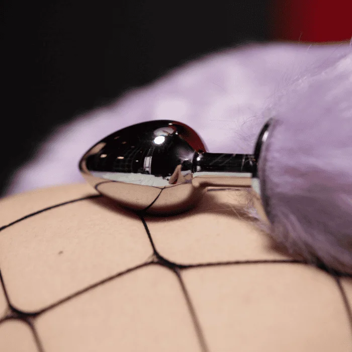 Μεταλλική πρωκτική σφήνα με μωβ γούνινη ουρά πάνω σε δίκτυο καλσόν.