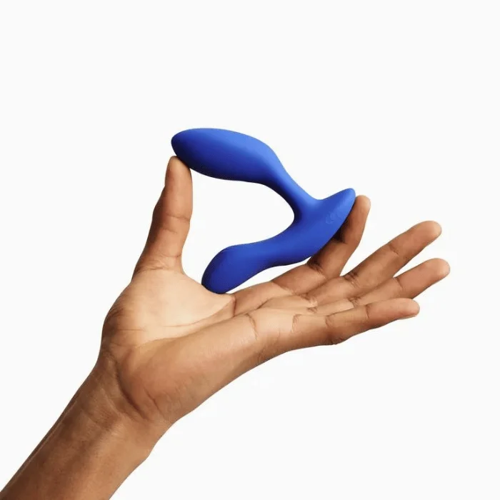 Χέρι κρατά μπλε πρωκτική σφήνα σιλικόνης σε λευκό φόντο με απαλό φωτισμό.