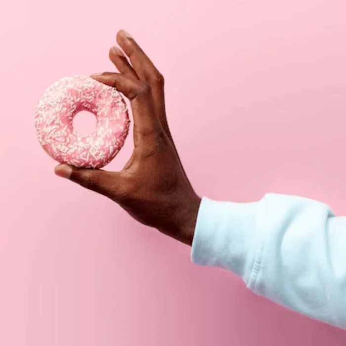 Χέρι που φοράει λευκό βαμβακερό φούτερ κρατά ροζ ντόνατ με τρούφα, μπροστά από ροζ background.