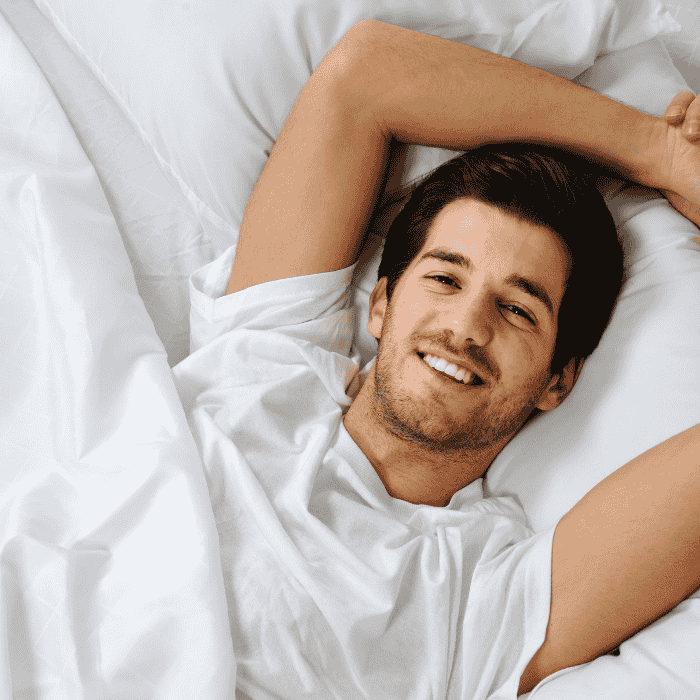 Χαμογελαστός άντρας ξαπλωμένος σε λευκά σεντόνια.