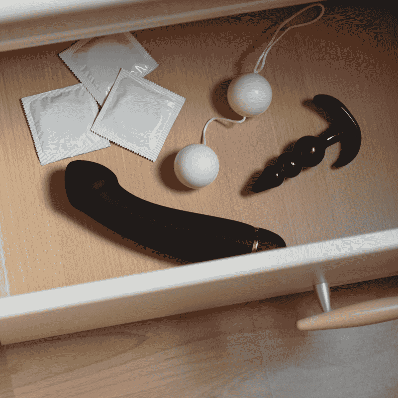 Συρτάρι Με Sex Toys Και Προφυλακτικά Ανοιχτό συρτάρι που περιέχει τρία προφυλακτικά, μπάλες kegel, έναν μαύρο κλασικό δονητή και μια μαύρη πρωκτική σφήνα με τρεις μπίλιες.