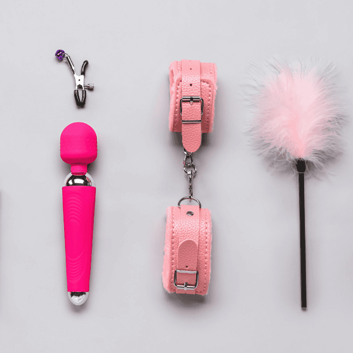 Ροζ Ερωτικά Αξεσουάρ Σε Σειρά σε Γκρι Φόντο Ροζ σετ με ερωτικά βοηθήματα (χειροπέδες, wand, tickler, σφιγκτήρας) πάνω σε γκρι φόντο, τακτοποιημένα με συμμετρική διάταξη.